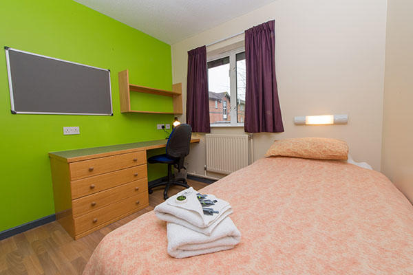 A bedroom inside 91 accommodation. There is a single bed, a large pin board, desk, chest of drawers and a window in the room.